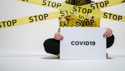 person holding card reading Covid-19 with yellow STOP tape on them